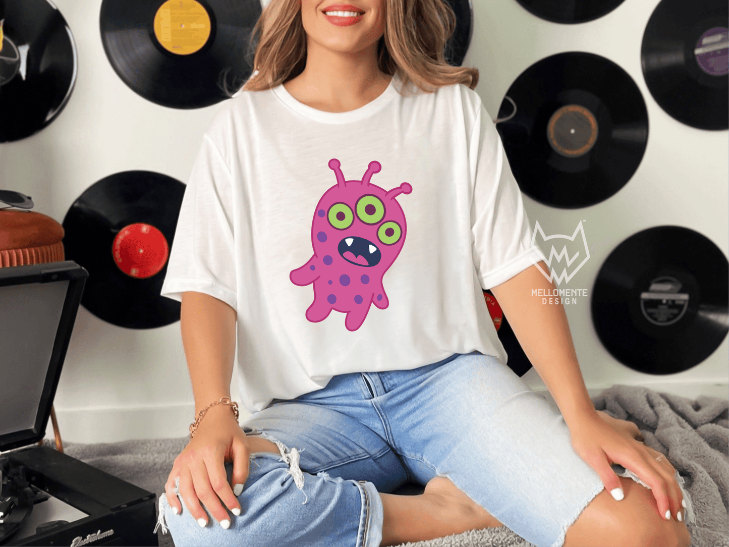 Woman wearing a white shirt featuring a pink alien creature against a wall with records.