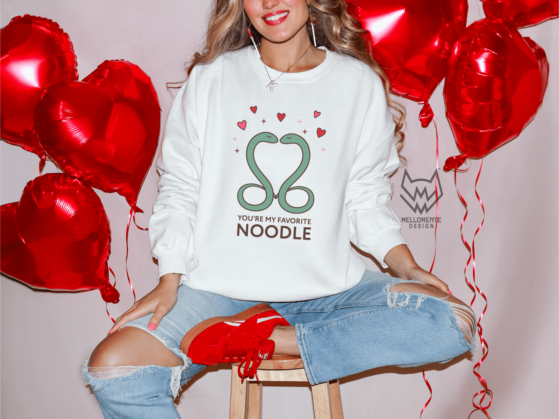 Woman wearing a white sweater featuring a cute valentine themed snake design captioned: "You're my favorite noodle."