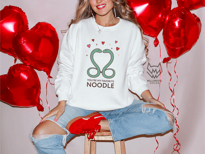 Woman wearing a white sweater featuring a cute valentine themed snake design captioned: "You're my favorite noodle."