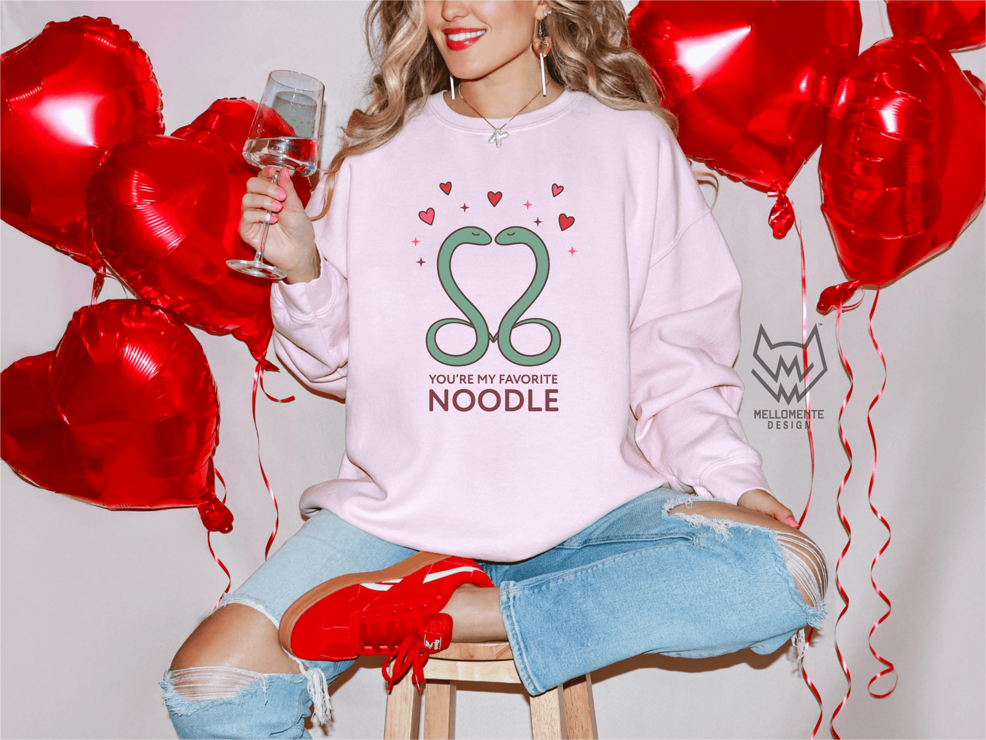Woman wearing a light pink sweater featuring a cute valentine themed snake design captioned: "You're my favorite noodle."