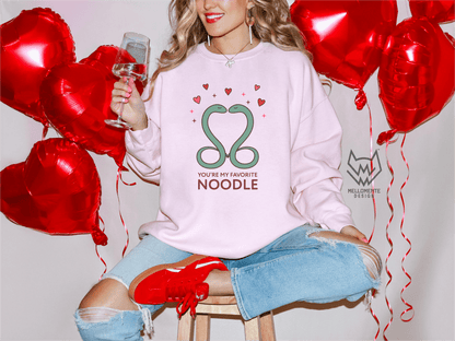 Woman wearing a light pink sweater featuring a cute valentine themed snake design captioned: "You're my favorite noodle."