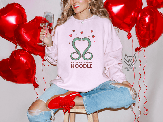 Woman wearing a light pink sweater featuring a cute valentine themed snake design captioned: "You're my favorite noodle."