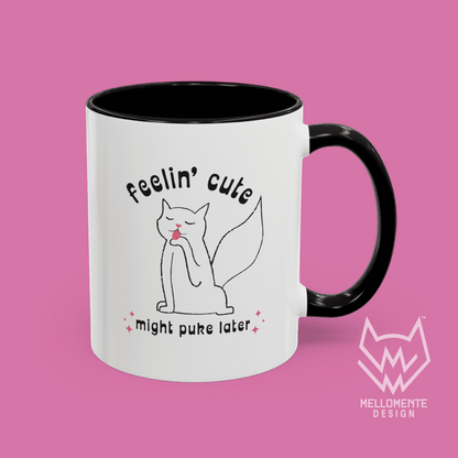 White mug with black interior featuring a cat illustration and text 'Feelin' cute might puke later' on a solid background.