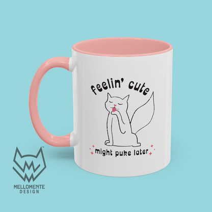 White mug with pink interior featuring a cat illustration and text 'Feelin' cute might puke later' on a solid background.
