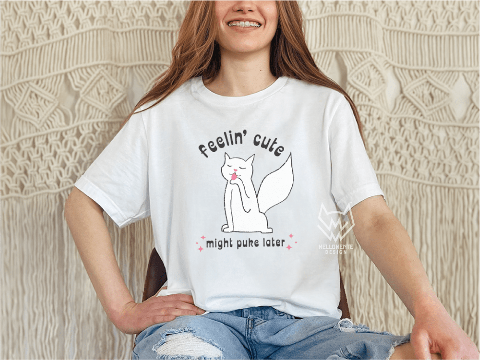 Person wearing a white t-shirt with a white cat graphic and text, sitting against a textured wall.