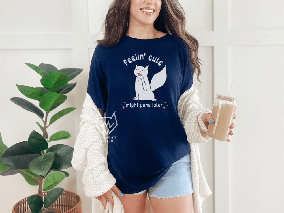 Woman wearing a navy blue shirt with a white cat graphic and text, holding a drink indoors.